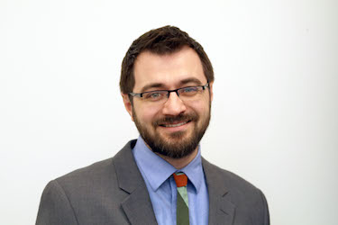 Professional headshot of Martin Donakowski wearing a grey suit, Blue shirt and green tie.