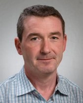 Thom Bateman's professional headshot wearing a grey collared shirt